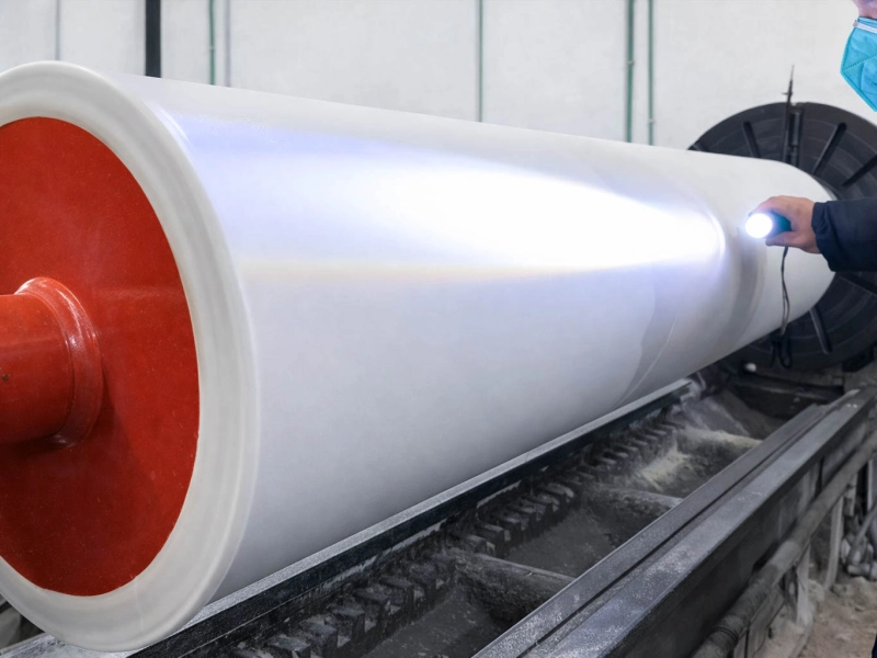 Worker inspecting a white rubber roller surface with a handheld light