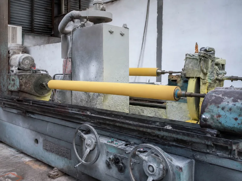Yellow Hypalon CSM rubber rollers being ground on a factory machine